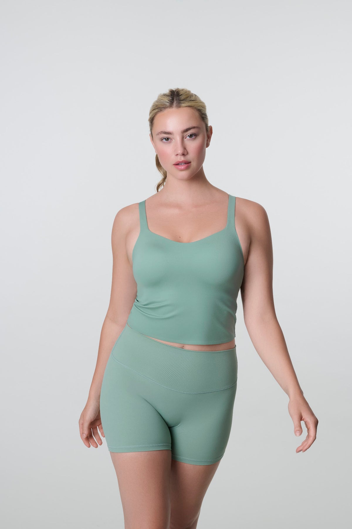 Model walking toward the camera in the HUUG Bra Tank in Sage with matching bike shorts