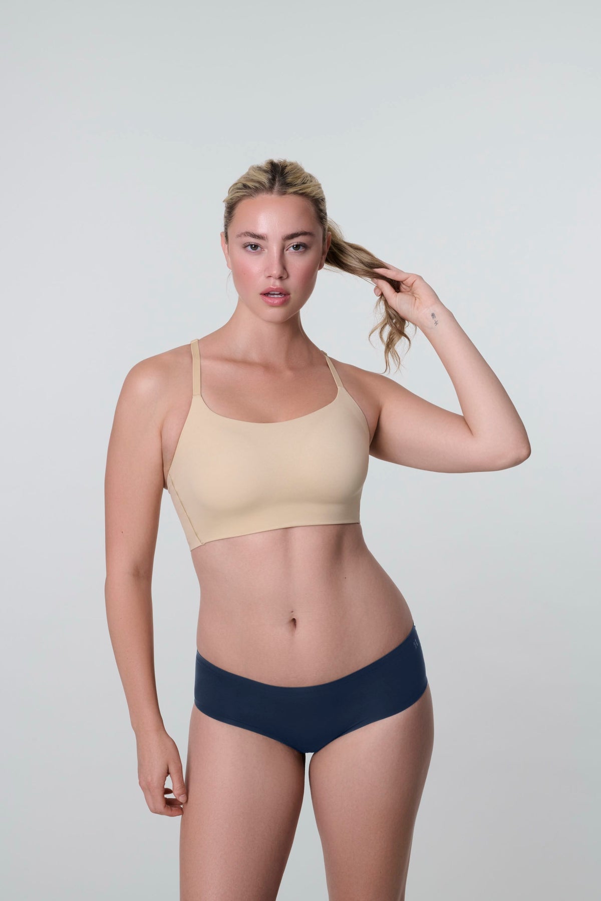 Daily Hipster in Navy, front view worn by a woman touching her ponytail, with a nude bralette