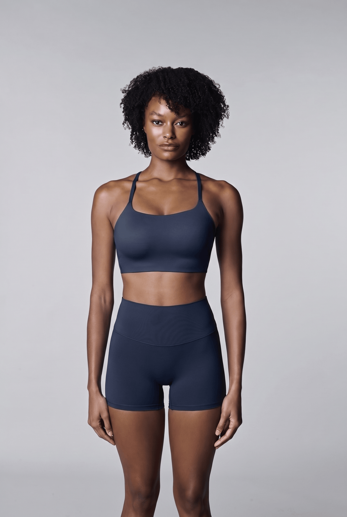 Bike Short in Navy, front view worn by a woman with short curly hair, with a matching navy racerback bra